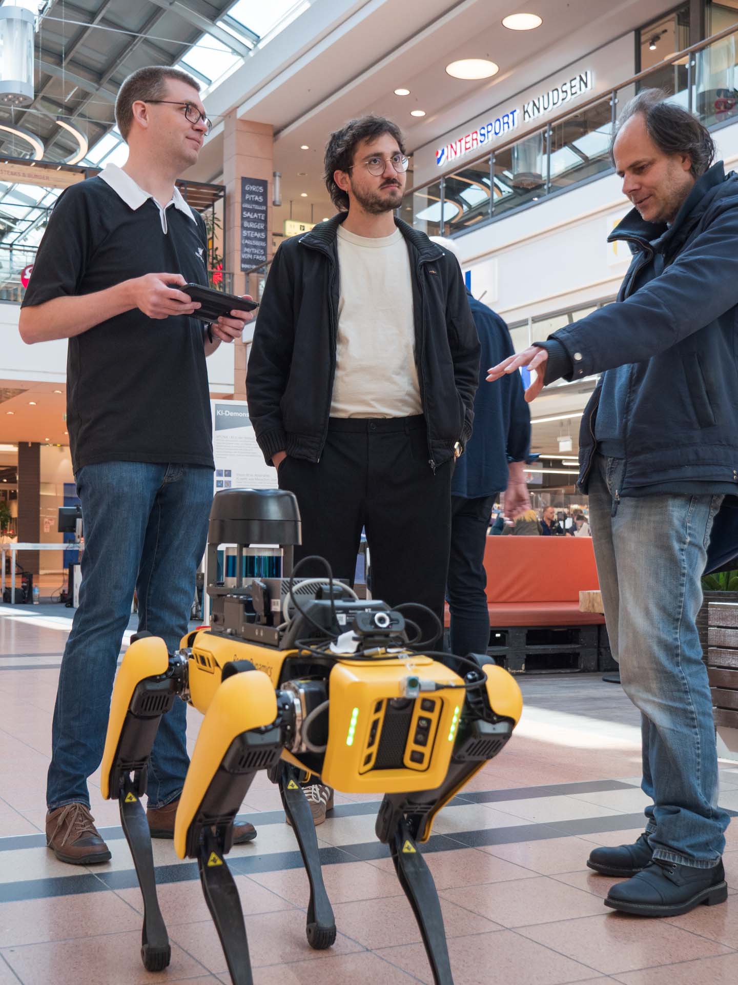 Drei Männer stehen in einem Einkaufzentrum um einem Roboter herum